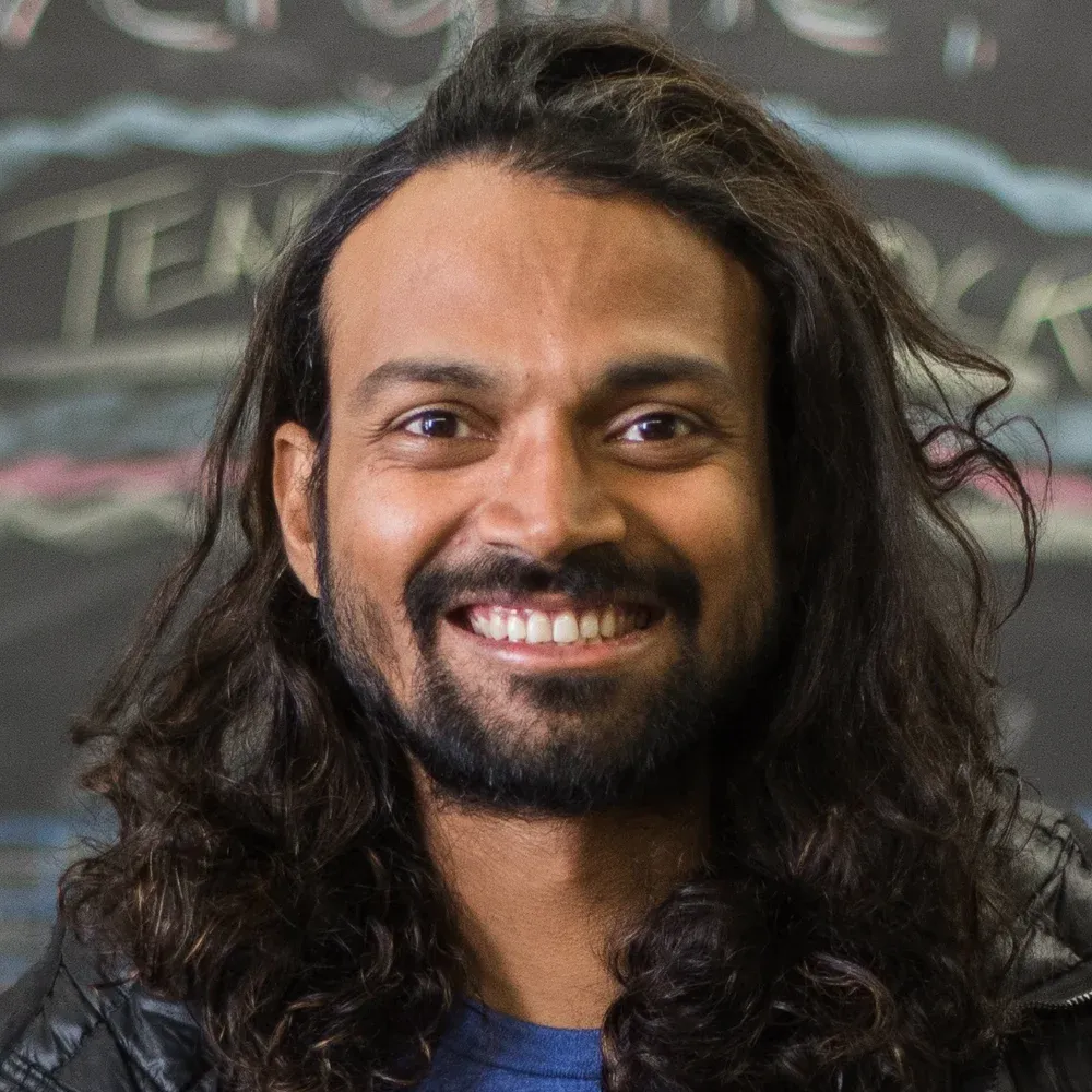 Naresh Kumar smiling, with long curly hair, in a black North Face jacket and a Bedrock Sandals T-shirt
