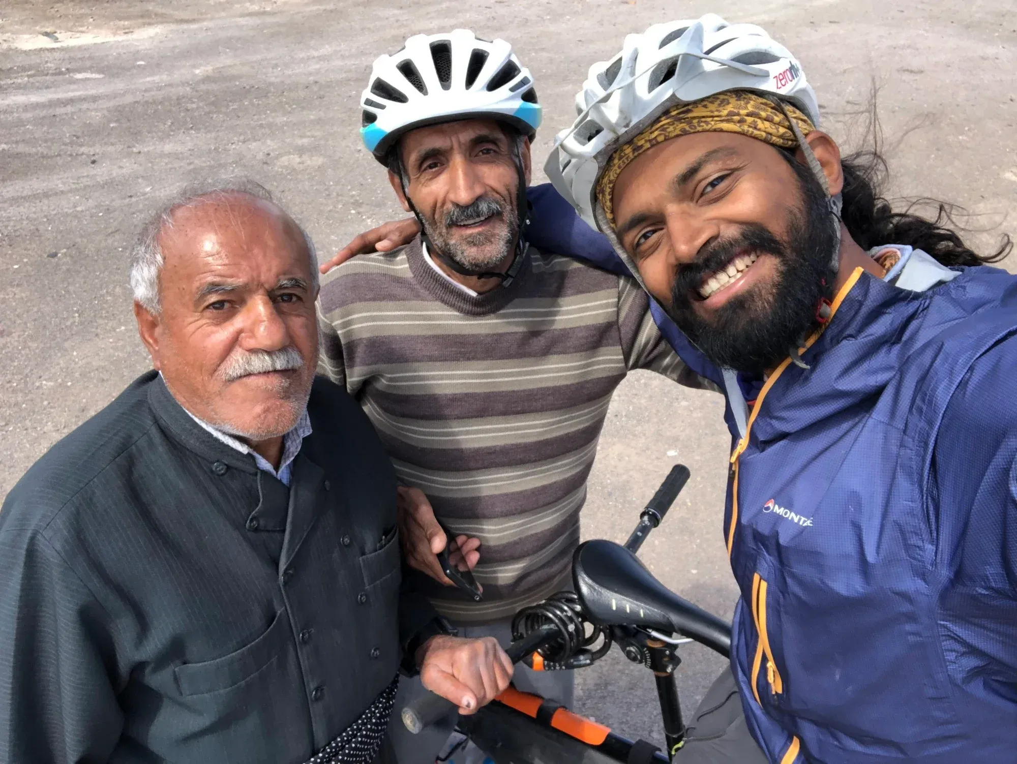 Naresh in a cycling helmet taking a selfie with two smiling older men